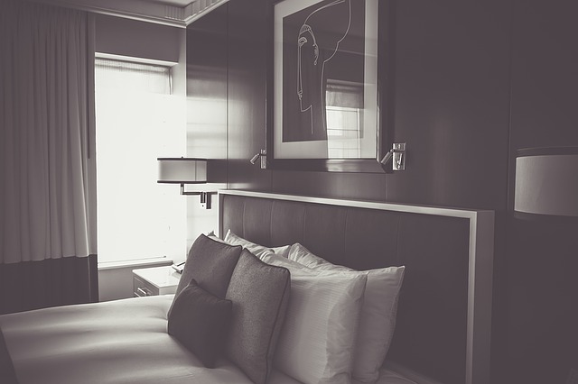 černobílá fotografie ložnice, postel, polštáře, obraz, lampy